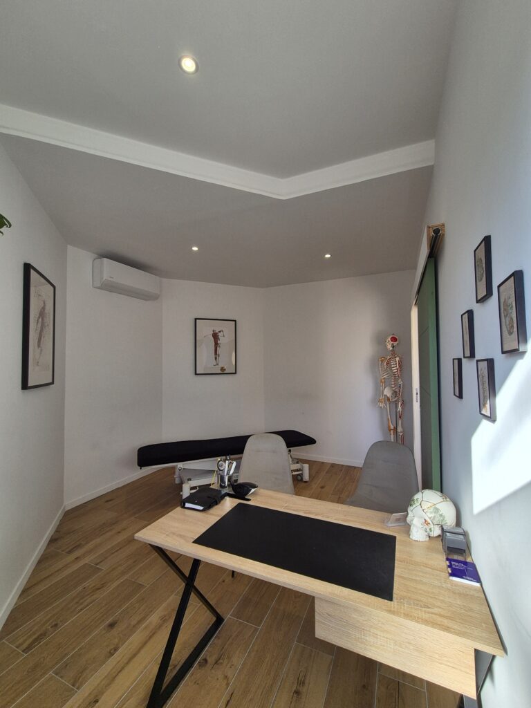 Vue du cabinet d’ostéopathie à Toulon depuis le bureau, avec la table de pratique, les chaises et la décoration.