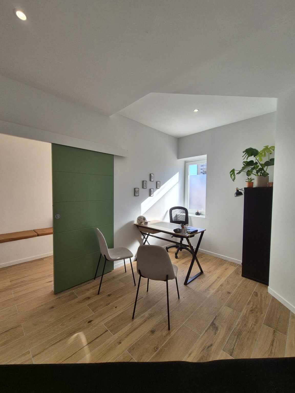 Vue du cabinet d’ostéopathie à Toulon depuis la table de pratique, montrant le bureau, la porte, la fenêtre, les chaises et la décoration.