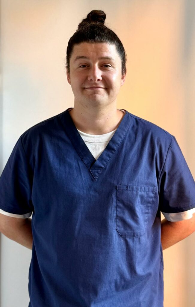 Portrait de Mario, ostéopathe à Toulon, debout en blouse et souriant.
